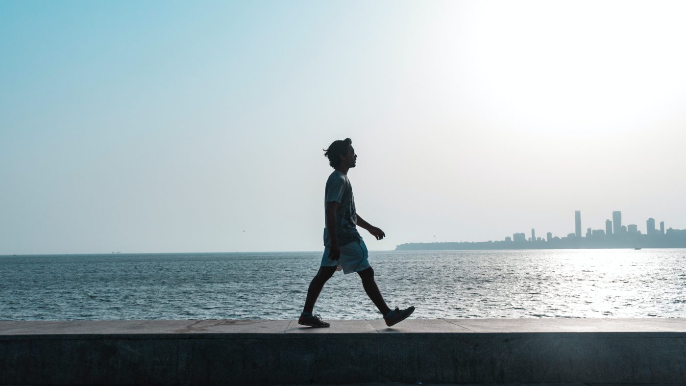 Ein Mann läuft entlang der Küste, im Hintergrund ist eine Großstadt