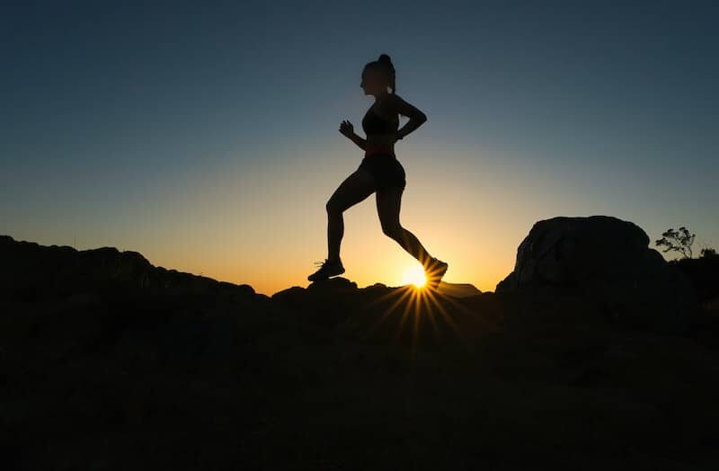 Eine Frau joggt in der Natur, man sieht im Hintergrund einen Sonnenuntergang.