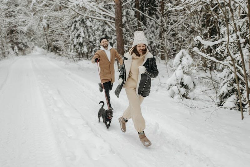 Ein Junge und ein Mädchen laufen mit ihrem Hund durch den Schnee, sie tragen Winterstiefel