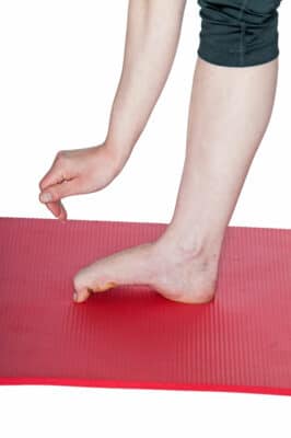 Das Bild zeigt eine Übung, mit der man die Schmerzen beim Knick-Senk-Spreizfuß durch das gezielte Stretchen der Fußmuskulatur lindern kann.