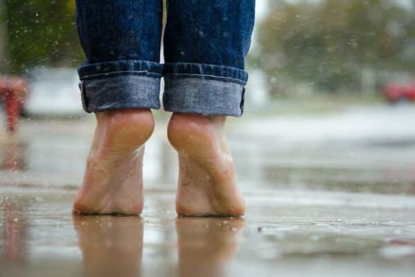 Ein paar Füße steht auf Zehenspitzen im Regen.
